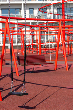 Swings and red metallic playground structures under clear light, captured in residential environment with urban architecture in Copenhagen, Denmark.