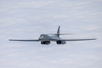 Side  view of a B-1 Lancer among clouds, with wings full forward