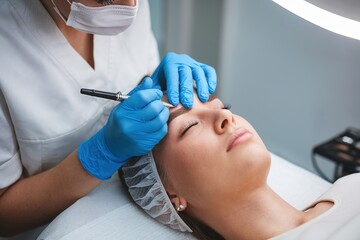Naklejka premium Professional Eyebrow Microblading Procedure: Beautician Performing Permanent Makeup Treatment in Beauty Salon