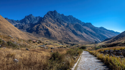 A stone pathway winds through a golden valley surrounded by majestic, rugged mountains under a clear blue sky, inviting exploration and adventure into nature's beauty.