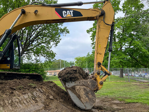 Springfield, Illinois, USA : May 6, 2024 Industrial bulldozer, excavator or backhoe uses a hydraulic arm with a scoop to move dirt and grass in a field. City location.
