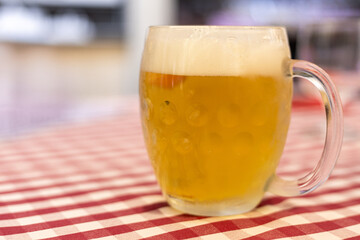 Refreshing mug of beer sitting on a checkered tablecloth in a lively dining area during an evening gathering