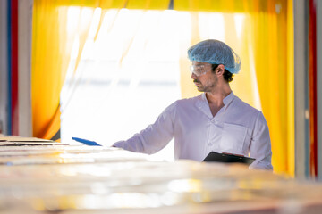 Food industry worker wearing hygiene gear inspects packaged products in a factory warehouse with...