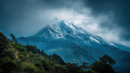 Fototapeta premium A majestic snow-capped mountain peak rises dramatically amidst the swirling clouds and lush green forest, showcasing the beauty of nature's powerful landscape.