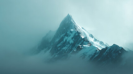 Majestic snow capped mountain peak emerges through a dense fog blanket on a cold winter day with a light dusting of fresh snow on the steep rock face.