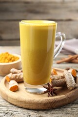 Delicious turmeric latte in glass cup, roots and anise star on wooden table, closeup