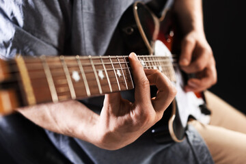 Fototapeta premium Man playing guitar on black background, focus on hand