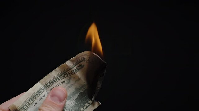 Partially Burned Fifty Dollar Bill with Large Flame Rising as Hand Holds Charred Currency over Black Background, Close Up Scene of Economic Symbolism