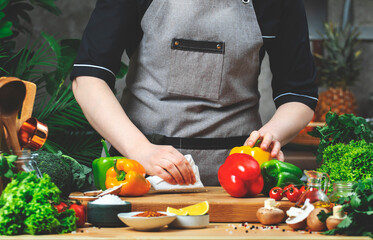 Cooking food in the kitchen. Chef sweeps food waste from the table with napkin. Wooden table, kitchenware, vegetables, herbs and ingredients. Healthy vegan eating, recipes, blogging
