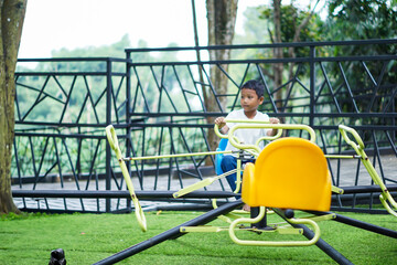 A young asian boy enjoys riding a colorful merry-go-round on a bright day at the outdoor playground.