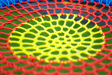 Close-up of a colorful woven net with yellow and red strings forming a circular geometric pattern.