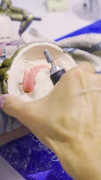 Close-up of a dental professional refining a pink acrylic partial denture using a rotary tool while it remains in the mold.