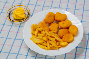 French fries and golden nuggets in a plate on a white checkered tablecloth