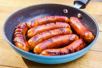 grilled sausages in a frying pan, on a wooden table