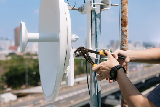 Selective focus to engineer's hands tightening the mounting nuts to install the Wi-Fi signal dish system.