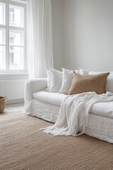 A white sofa with a tan throw blanket and pillows sits on a tan rug in a minimalist living room