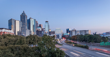 Downtown Atlanta Skyline showing several prominent buildings, highways, cars, light trails and hotels under a blue sky.