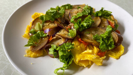 Top view of stir-fried eggplant and chili served over fluffy scrambled eggs, garnished with fresh lettuce on white plate