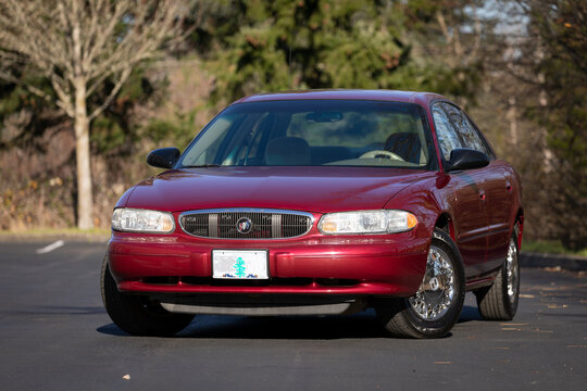 Portland, OR, USA - Dec 5, 2020 - 2003 burgundy Buick Century sedan parked on asphalt. American four-door passenger car with chrome wheels, compact body, and vintage design in suburban area