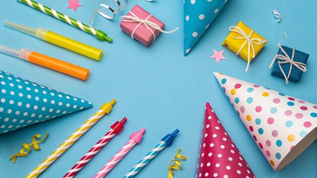 Colorful birthday party decorations with polka dot hats, candles, and gift boxes arranged on a blue background