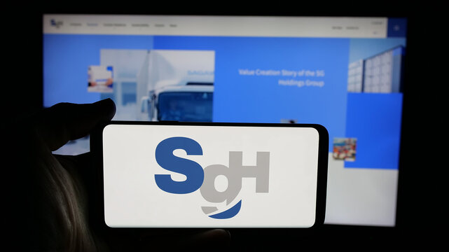 Stuttgart, Germany - 04-26-2025: Person holding cellphone with logo of logistics company SG Holdings Co. Ltd. on screen in front of webpage. Focus on phone display.
