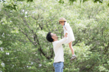 緑の背景で公園で娘を抱っこして高い高いする父親　と娘の親子の幸せや未来、幸福のイメージ