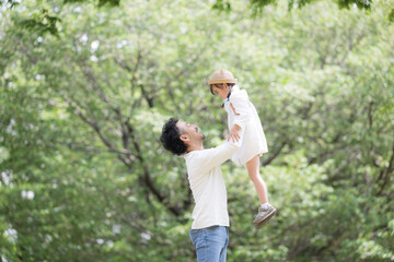 Fototapeta premium 緑の背景で公園で娘を抱っこして高い高いする父親 と娘の親子の幸せや未来、幸福のイメージ