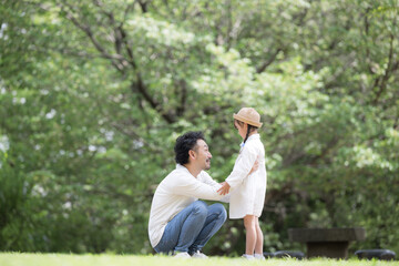 Naklejka premium 緑の背景で公園で娘と話す父親と娘の親子の幸せや未来、幸福、見守るや子育てなどのイメージ