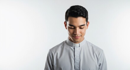 Obraz premium Portrait of a young man in a clerical collar looking down with a soft smile on a white background