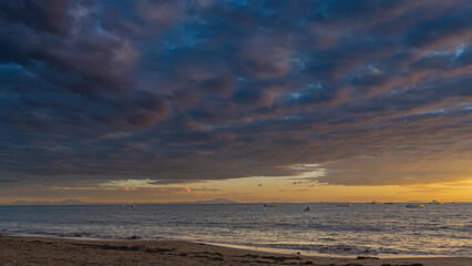 Beautiful tropical sunset over the ocean. The evening sky is orange on the horizon. Blue clouds are highlighted in pink. The boats are anchored in the sea. Sandy beach. Madagascar. Nosy Be  