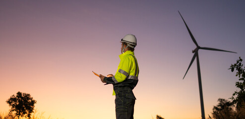Engineer man working with tablet at windmill farm Generating electricity clean energy. Wind turbine farm generator by alternative green energy. © Nabodin