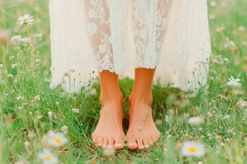 A person's feet resting on the grass. Green grass female legs. Female legs  and fresh flower.A person walking barefoot on grass, highlighting the sensory connection with earth.