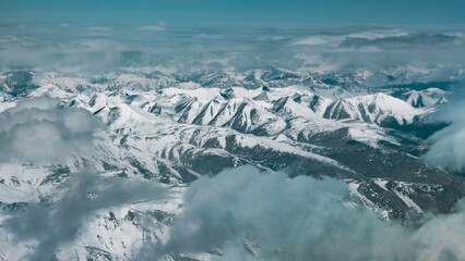 breathtaking aerial view of the snow covered peaks of the Himalayas, showcasing dramatic cliffs, deep valleys and serene glaciers under blanket of clouds in the world highest mountain range
