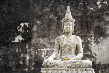 Fototapeta premium White Stone Buddha statue in meditation pose against old ruined wall. Copy space religious calmness background