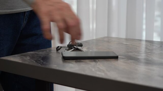 Hand grabbing smartphone and wallet from table near bright window.