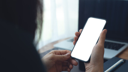 Naklejka na ściany i meble Mockup, Woman using mobile phone with blank white screen while online working on laptop at coffee shop. Business woman using smartphone, mockup for mobile app marketing, closeup