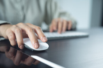 Woman hand clicking computer mouse on office table. Business woman working on desktop computer and using wireless mouse, browsing the internet, searching the information, business background, closeup