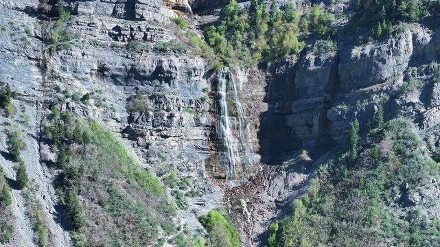 Aerial mountain Bridal Veil Falls Provo Utah 1 pull. 607 foot tall double cataract waterfall in Provo Canyon. Rugged rocky ledges and cliffs over pine forests. Deep canyon valley. Summer.