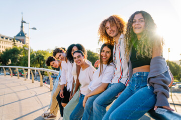Happy multi ethnic friends leaning on a railing, enjoying a sunny day in the city, capturing moments of laughter and connection together