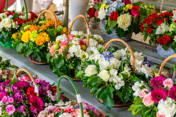 you can see various flower arrangements arranged in wicker baskets. Among the flowers you can see, among others, roses, gerberas, daisies and other seasonal ornamental plants. The arrangements are ric
