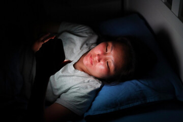 Asian woman using smartphone in bed at night: sleep deprivation and technology addiction