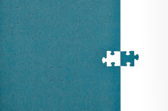 Teal jigsaw puzzle with one missing piece placed on the side over a brown background.