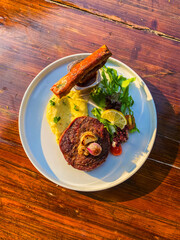 Close-up of gourmet beef dish presented on a white plate, placed on a wooden table, showcasing the culinary artistry and attention to detail.