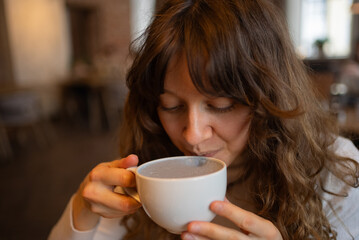 Young woman savors the unique flavor of a charcoal latte, a trendy beverage known for its health benefits and distinctive black color, in the warm atmosphere of a modern cafe