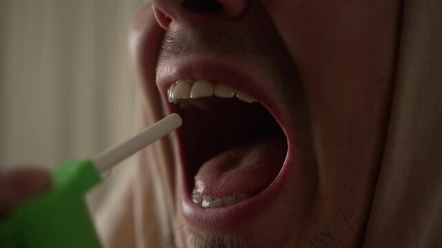 Close-up of a man spraying throat with oral antiseptic spray for sore throat relief and personal healthcare at home. Treatment of viral infection or sore throat at home.