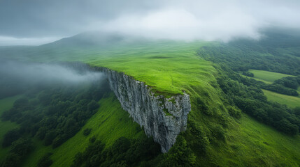 Lush green cliff with misty clouds hovering above, showcasing nature beauty and serenity