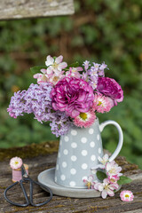 Blumenstrauß mit lila Ranunkeln, Flieder, Gänseblümchen, Hasenglöckchen und Zierapfel-Blüten im Milchkännchen