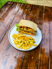 Vertical shot of a sandwich and fries on a blue rimmed plate, displayed on a wooden table in a...