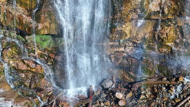 Aerial climb lower Bridal Veil Falls rainbow Provo close 1 Utah. 607 foot tall double cataract waterfall in Provo Canyon. Rugged rocky ledges and cliffs over pine forests. Deep canyon valley. Summer.