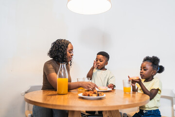 Cheerful african family enjoying breakfast together at home, sipping orange juice and indulging in sweet donuts, creating joyful memories